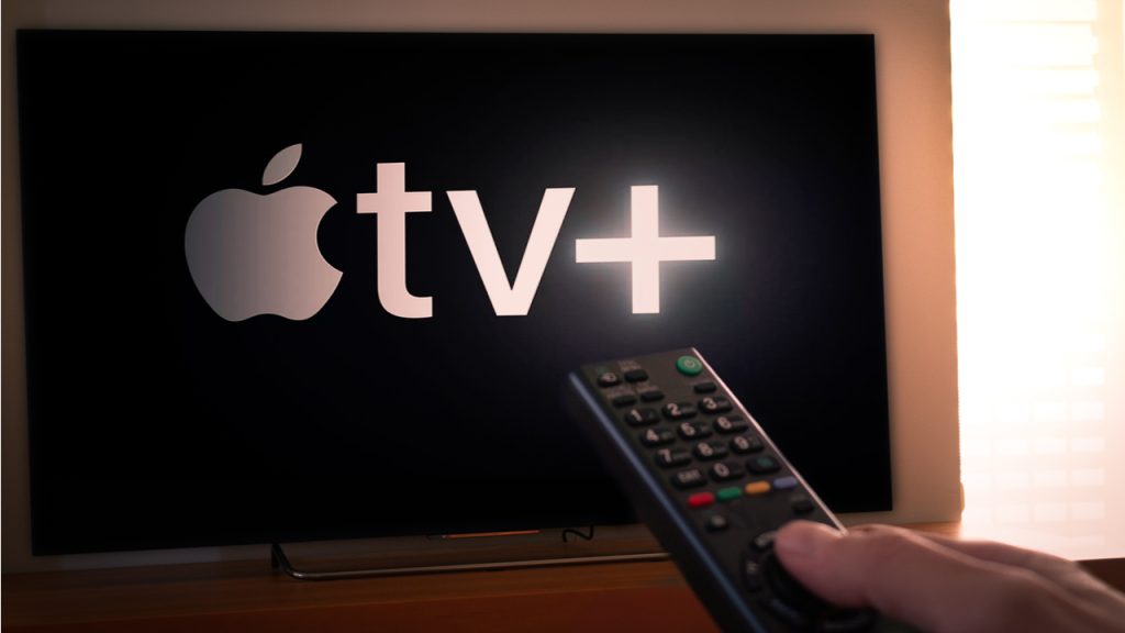 Man holds a remote control With the new Apple TV+ screen on TV.